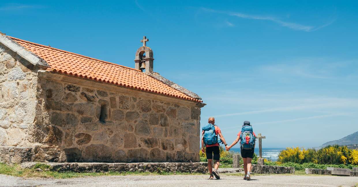 Couple of pilgrims walking next to old church on Camino Portuguese Way